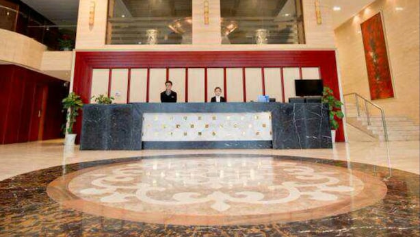 A hotel reception area with a marble floor, a large chandelier, and a reception desk with two staff members. - K Raphael Hotel (Xi'an)