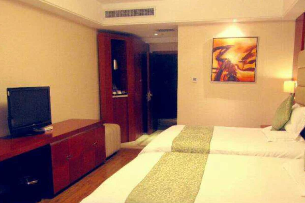 A hotel room with two beds, a TV, a wardrobe, and a painting on the wall.