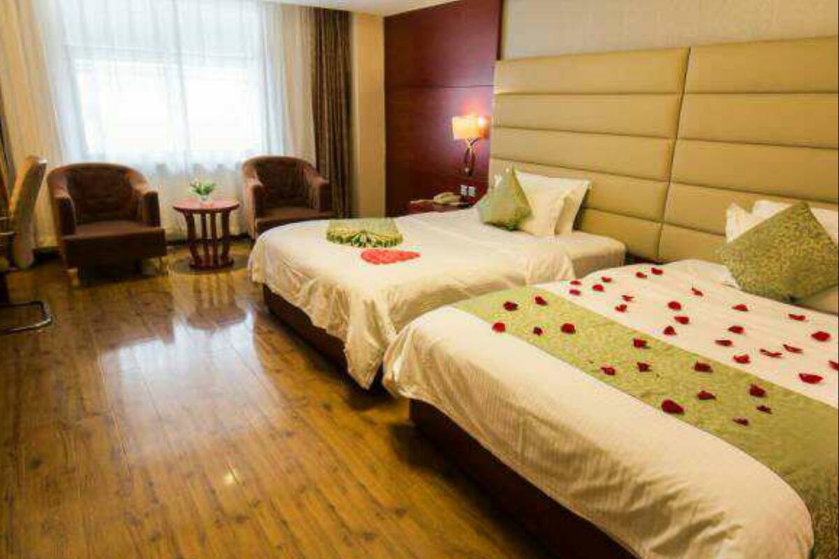 A hotel room with two beds, a wooden floor, a sitting area with chairs, and a large window with curtains.