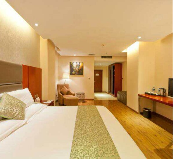 A hotel room with a large bed, a desk, a chair, and a small table.