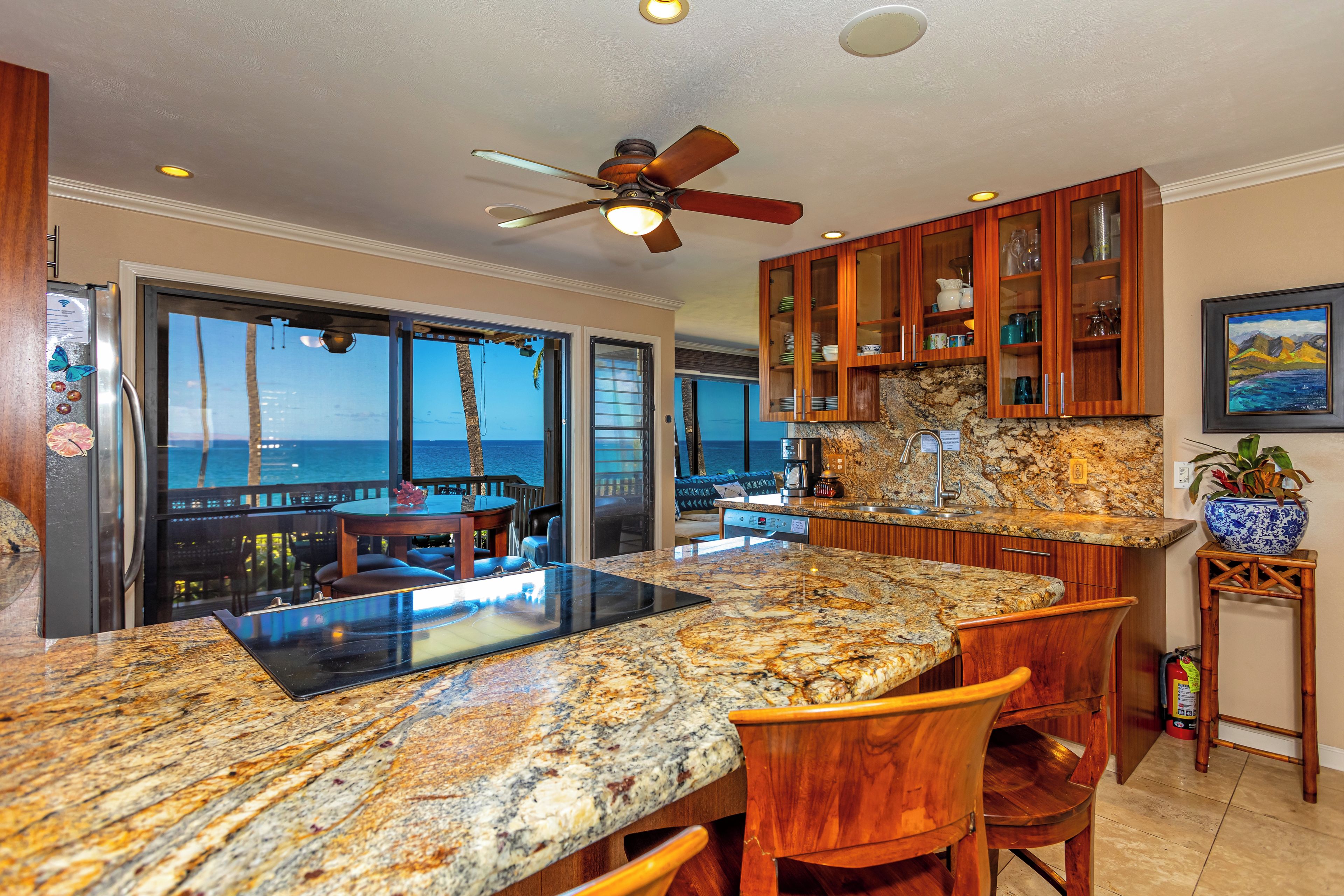A kitchen with a granite countertop, wooden cabinets, and a view of the ocean.