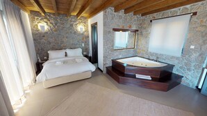 A bedroom with a stone wall, a large bed, a wooden ceiling, and a modern bathroom with a freestanding bathtub.