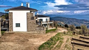 A modern two-story house with a stone facade, a flat roof, and a view of the surrounding landscape.