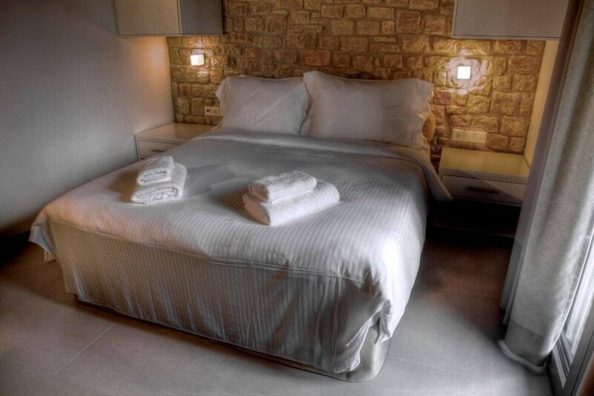 Een opgemaakt bed met gevouwen handdoeken, een stenen muur en nachtlampjes.