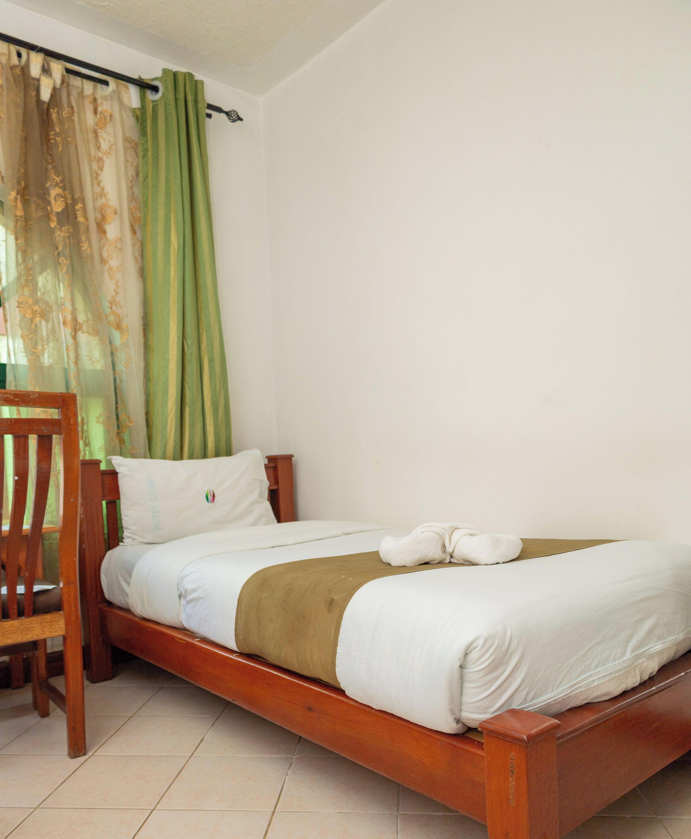 A single bed with a wooden frame, a white pillow, and a brown blanket.