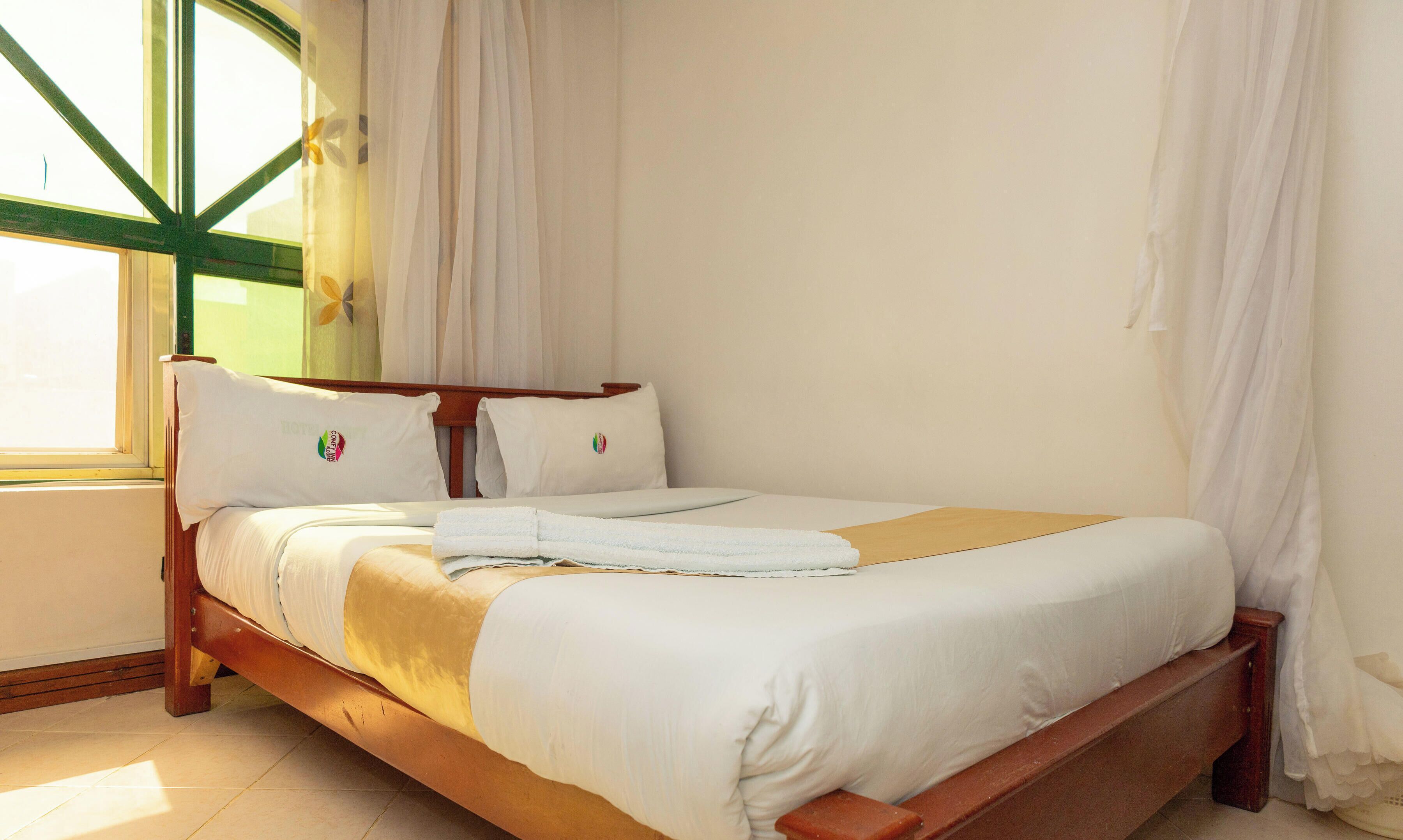 A single bed with a wooden frame, white bedding, and a window with curtains.