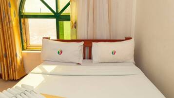 Habitación de hotel con cama, almohadas, ventana con cortinas y vistas al exterior.