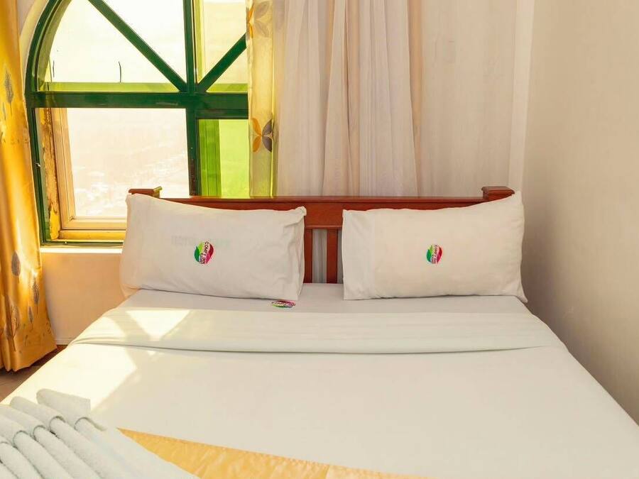 Habitación de hotel con cama, almohadas, ventana con cortinas y vistas al exterior.