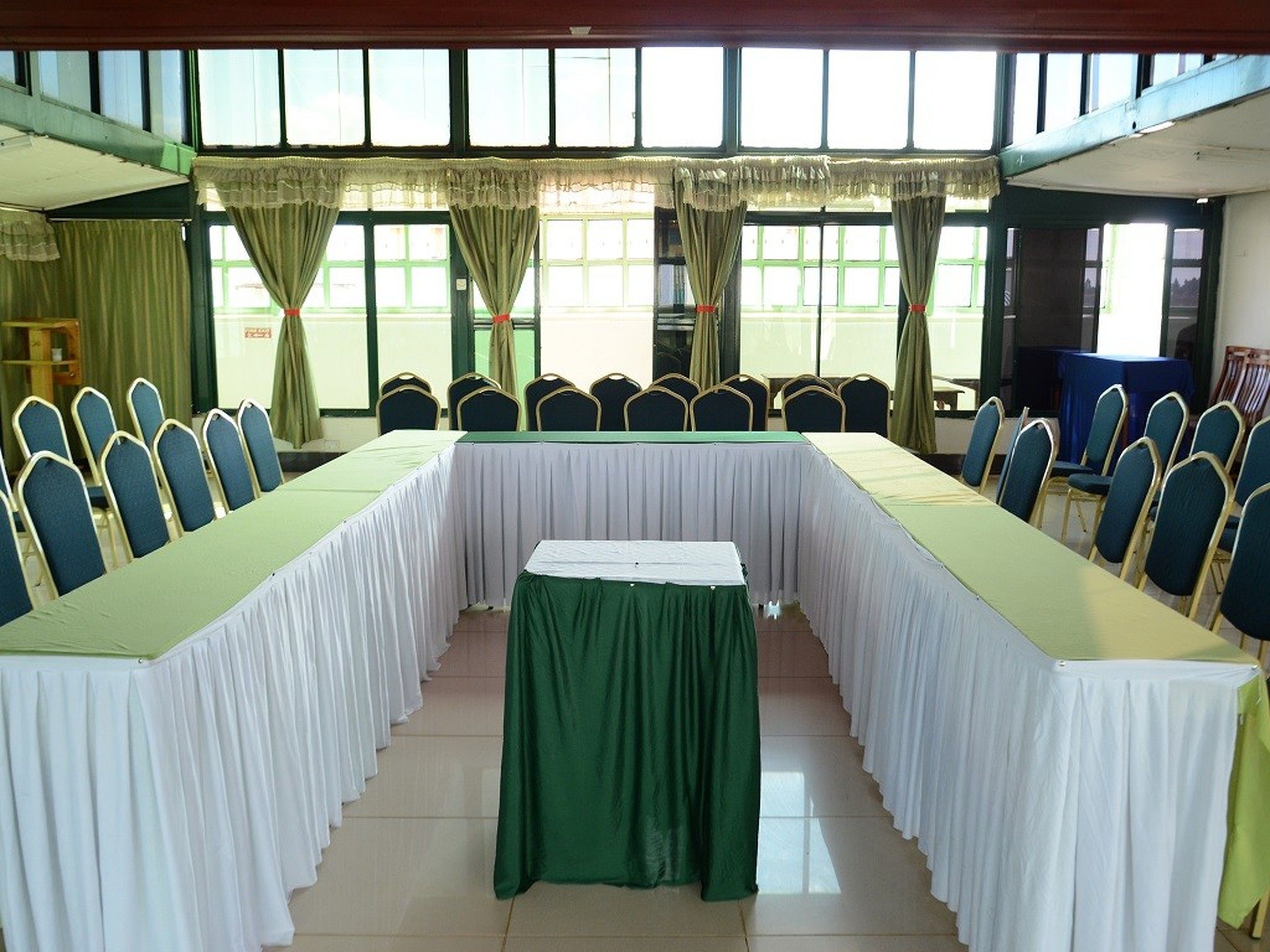 Uma sala de conferências com uma mesa comprida e cadeiras, janelas amplas e cortinas.