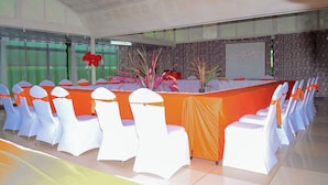 A conference room with a long table, white chairs with orange sashes, and potted plants. - Comfy Inn Eldoret (Eldoret)
