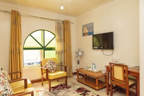 Una sala de estar con un ventanal grande, un televisor montado en la pared, un ventilador y una mesa de madera con sillas.