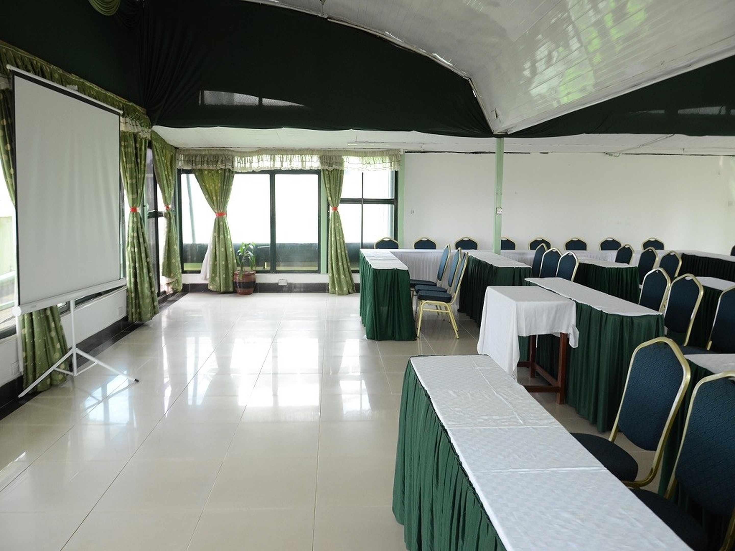 Une salle de conférence équipée d’un tableau blanc, de rideaux verts et de tables avec des chaises.