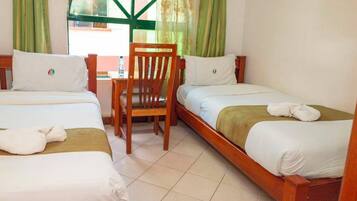 A hotel room with two single beds, a wooden chair, a small table, and a window with green curtains.
