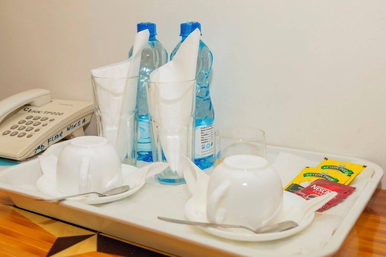 A tray with a telephone, two bottles of water, a glass, a cup, a spoon, and packets of coffee and tea.