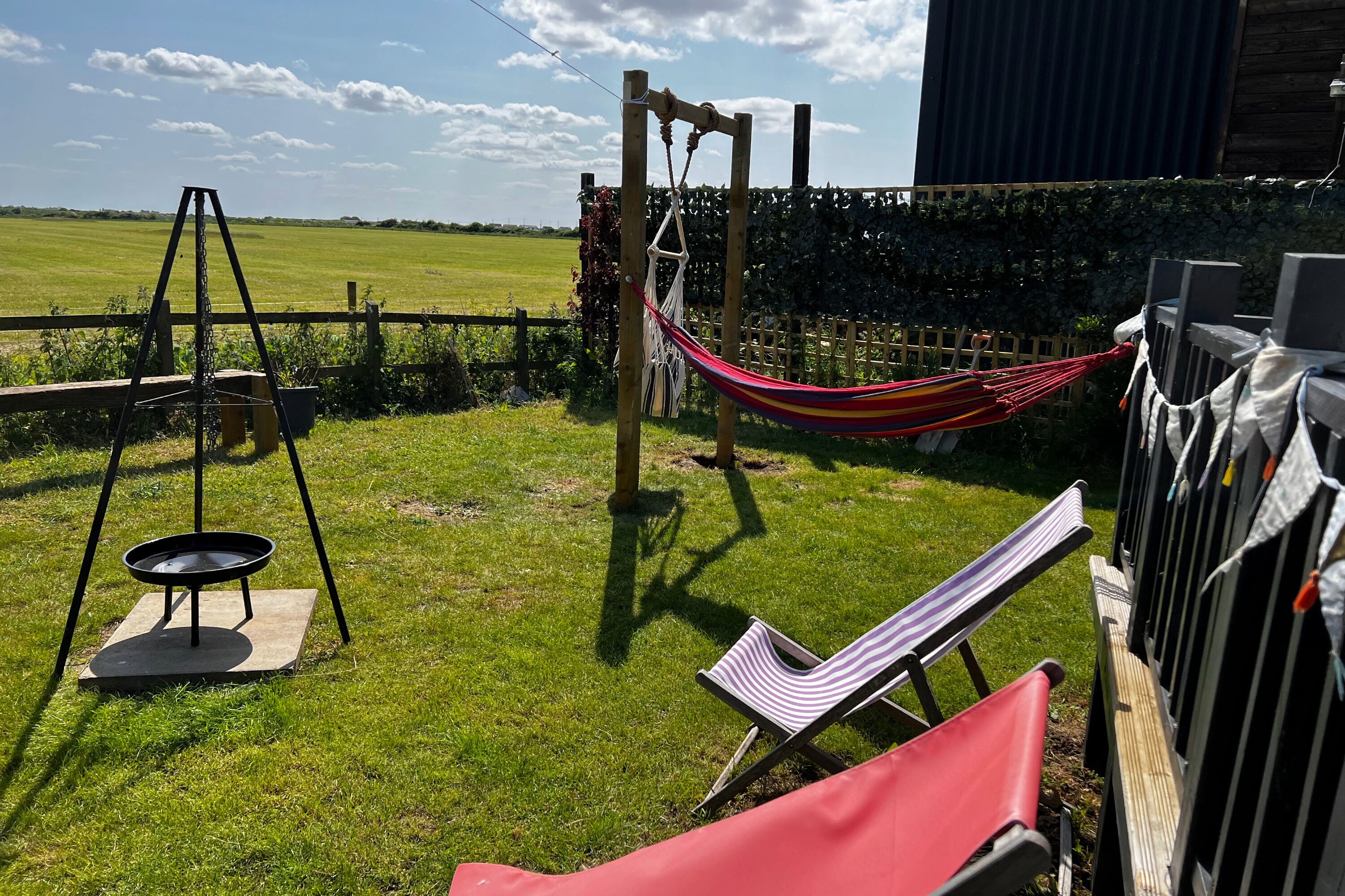 A hammock, swing set, and two striped lounge chairs in a grassy outdoor area with a view of a field.