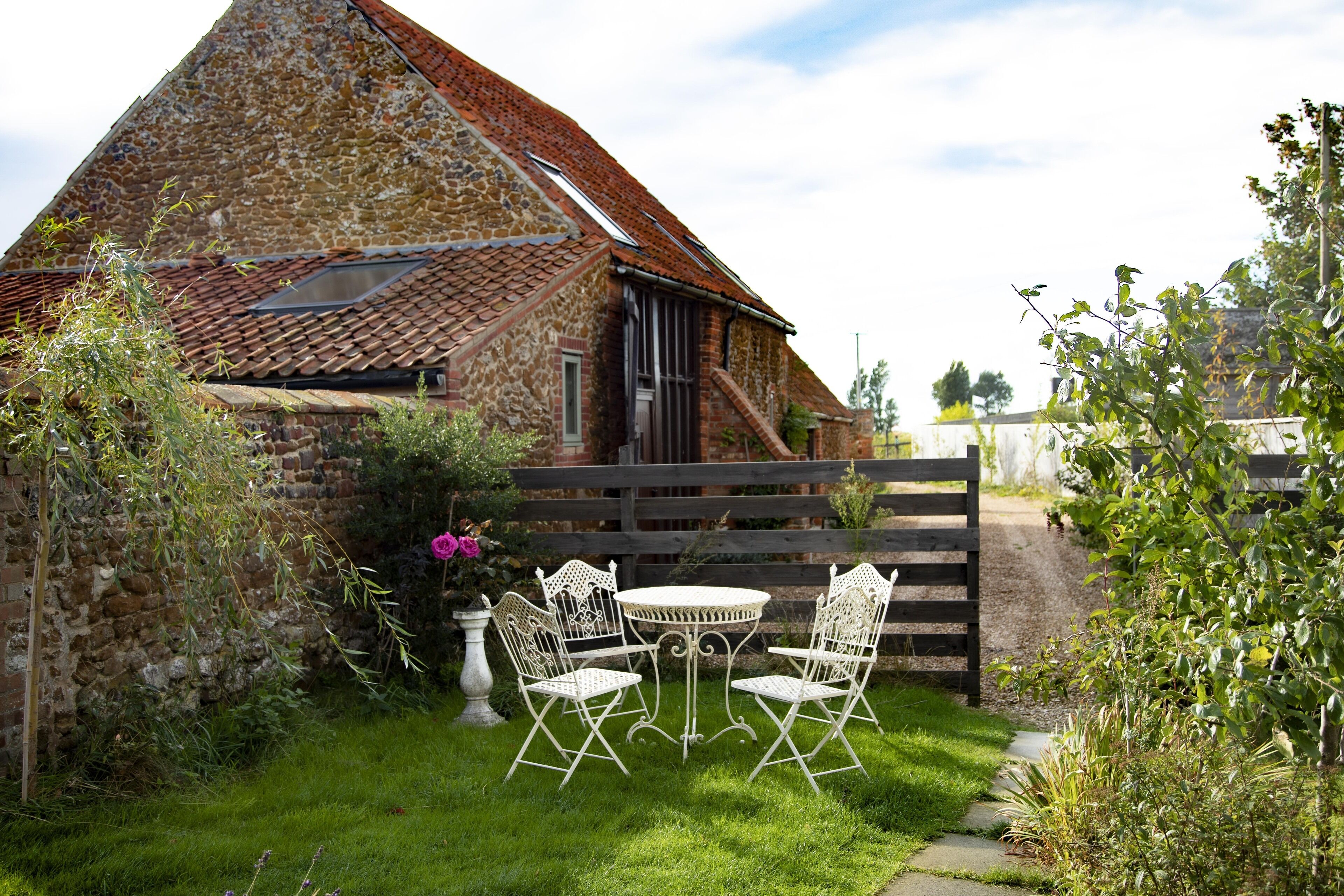 Een gebouw van steen met een pannendak, een houten omheining en een kleine tuin met een tafel en stoelen.