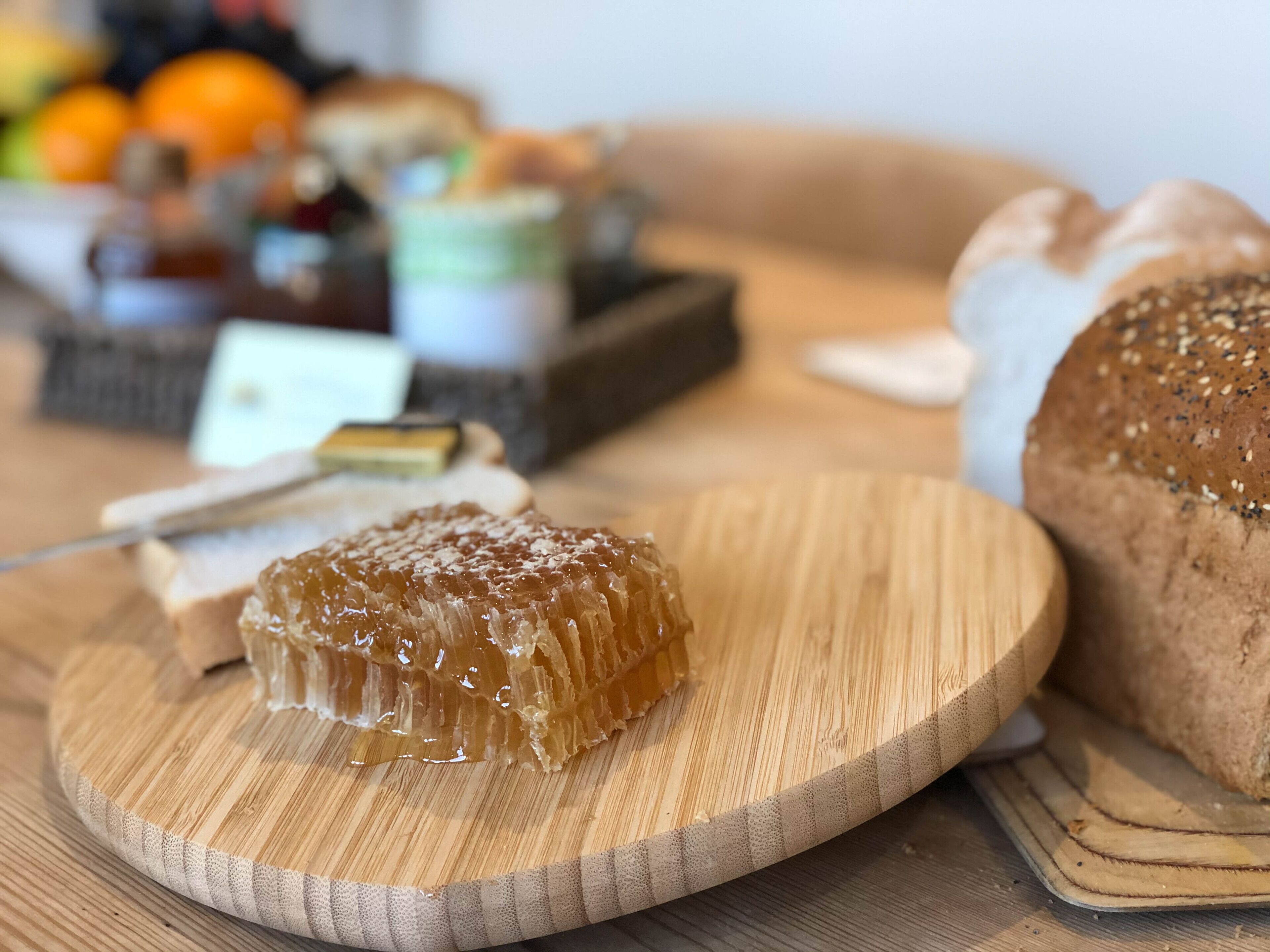 Un tagliere di legno con struttura a nido d'ape, una pagnotta e, sullo sfondo, un cesto di frutta.