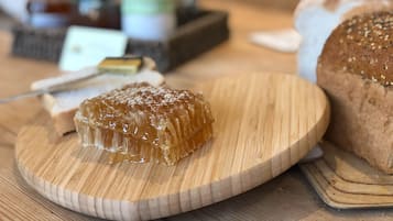 A wooden board with a honeycomb structure, a loaf of bread, and a basket of fruits in the background.