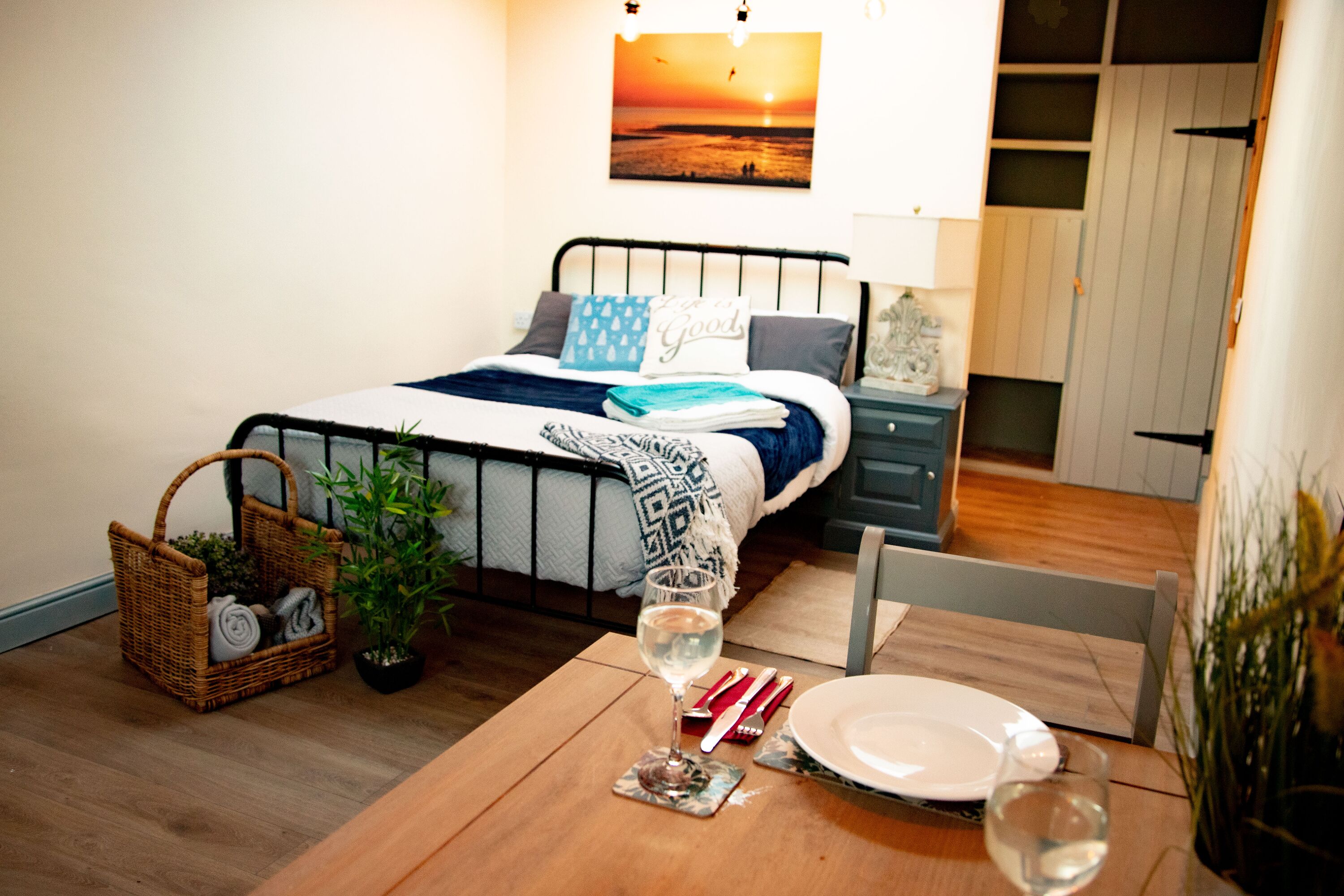 A bedroom with a bed, bedside table, and a dining table with a glass of water and a plate.
