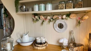 Una zona de cocina con estantes que contienen frascos, una cafetera y un espejo decorativo.