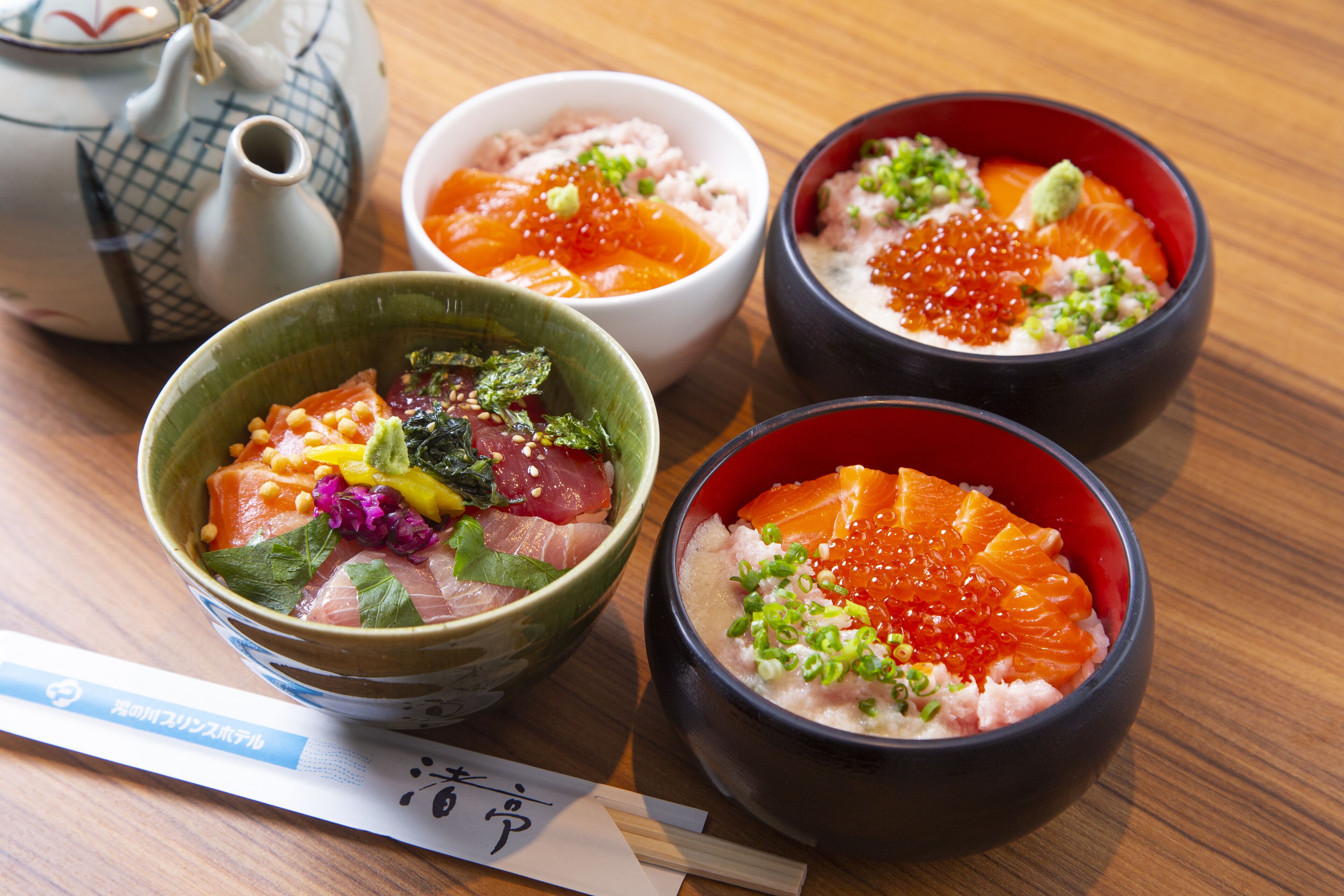 Three bowls of sashimi with salmon and roe, a teapot, and chopsticks on a wooden table.