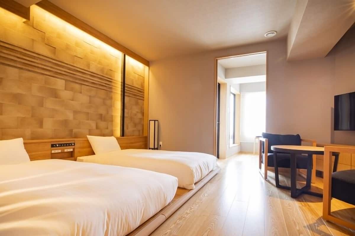 Una habitación de hotel con dos camas, un cabecero de madera, un escritorio con una silla y un televisor.