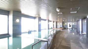 Una amplia piscina interior con agua cristalina, rodeada de paredes y bancos de azulejos.