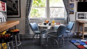 A dining area with a round table, four chairs, and a breakfast setup including fruits and a coffee mug. - Close to National Parks.The Star Garage, Sleep in a Vintage Truck Bed, Cool! (Kanab)
