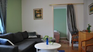 A living room with a grey sofa, a white coffee table, a blue vase with plants, a painting on the wall, and a wooden cabinet.