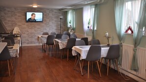 A dining area with tables and chairs, a television mounted on the wall, and a window with curtains.