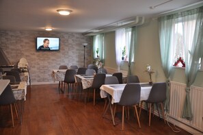 A dining area with tables and chairs, a television mounted on the wall, and a window with curtains. - Roddaren Vandrarhem - Hostel (Stromstad)