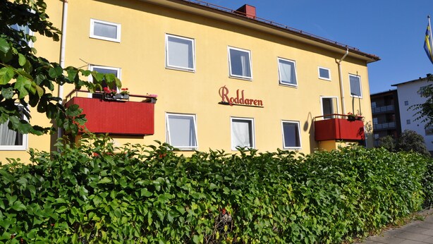 A yellow building with the name "Roddaren" on the facade, multiple windows, and a red balcony.