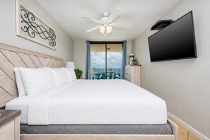 A hotel room with a bed, a ceiling fan, a TV, and a view of the outdoors. - BEACH Vacation! 2BR @ Phoenix V (Orange Beach)