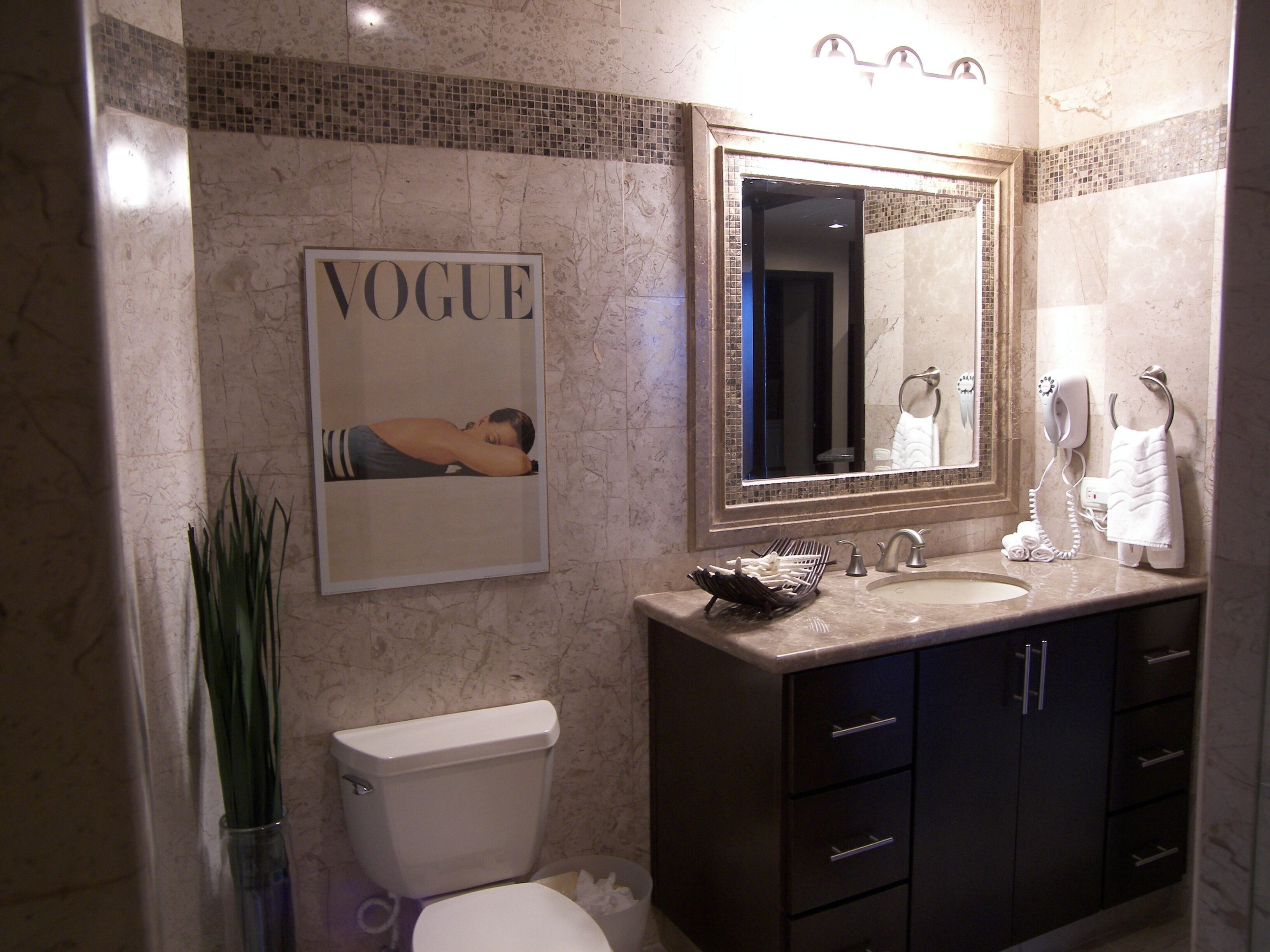 A bathroom with a toilet, sink, and mirror. There is a 'Vogue' magazine on the wall and a towel rack with towels.
