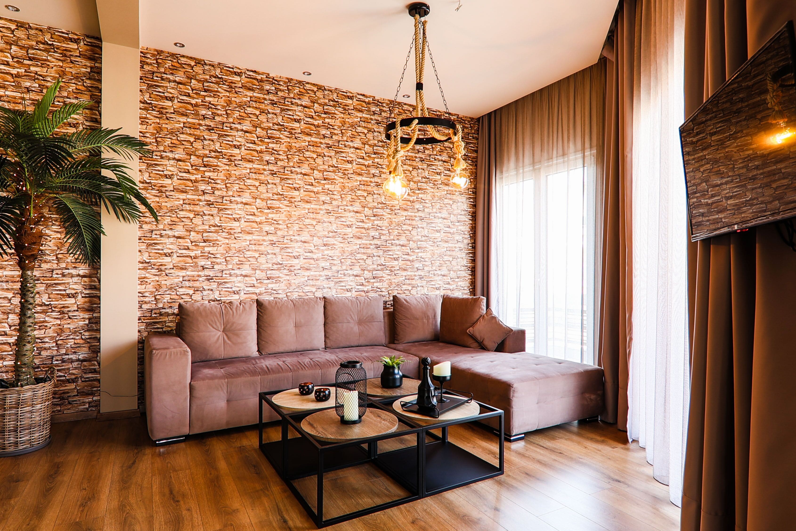 A modern living room with a stone wall, a brown leather sofa, a coffee table, and a hanging light fixture.