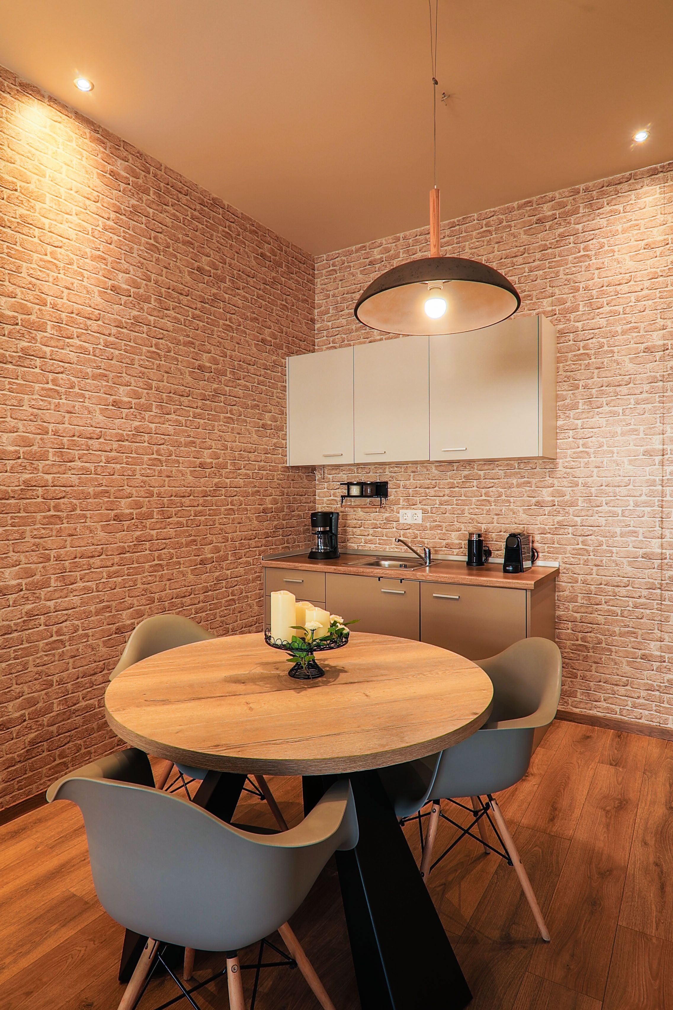 A dining area with a brick wall, a round wooden table, and modern chairs.
