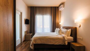 A hotel room with a large bed, a TV mounted on the wall, and a window with curtains.