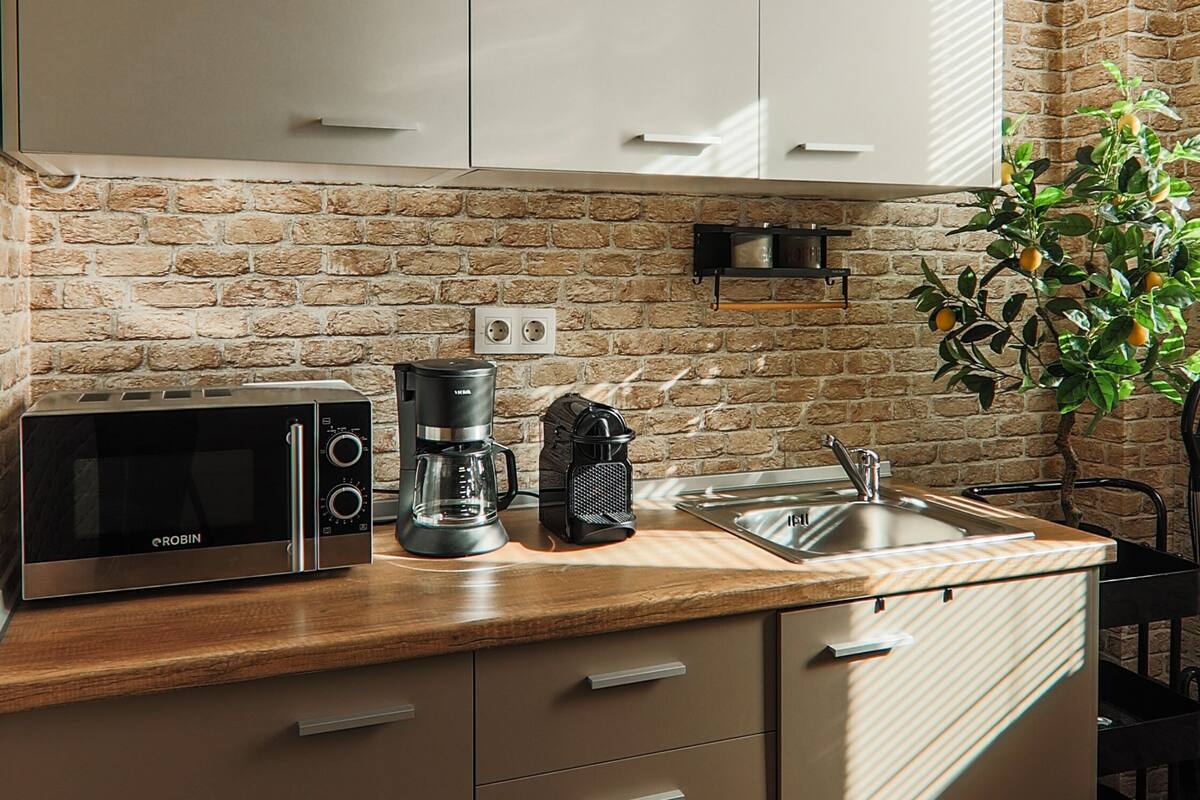 A kitchen with a brick wall, a microwave, a coffee maker, a sink, and cabinets.