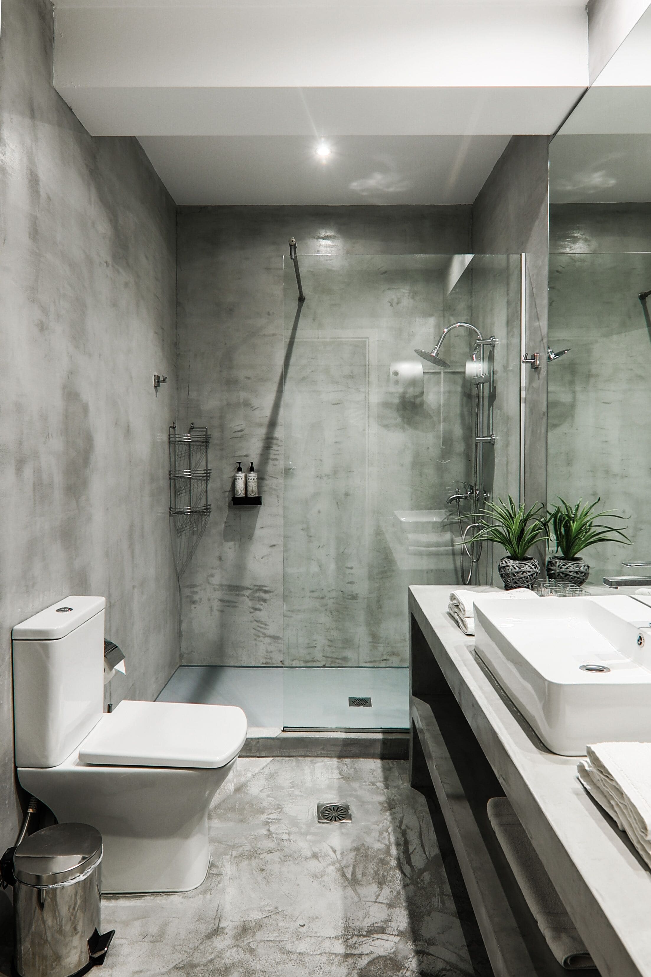 A modern bathroom with a shower, toilet, and sink, featuring a concrete wall and minimalist design.