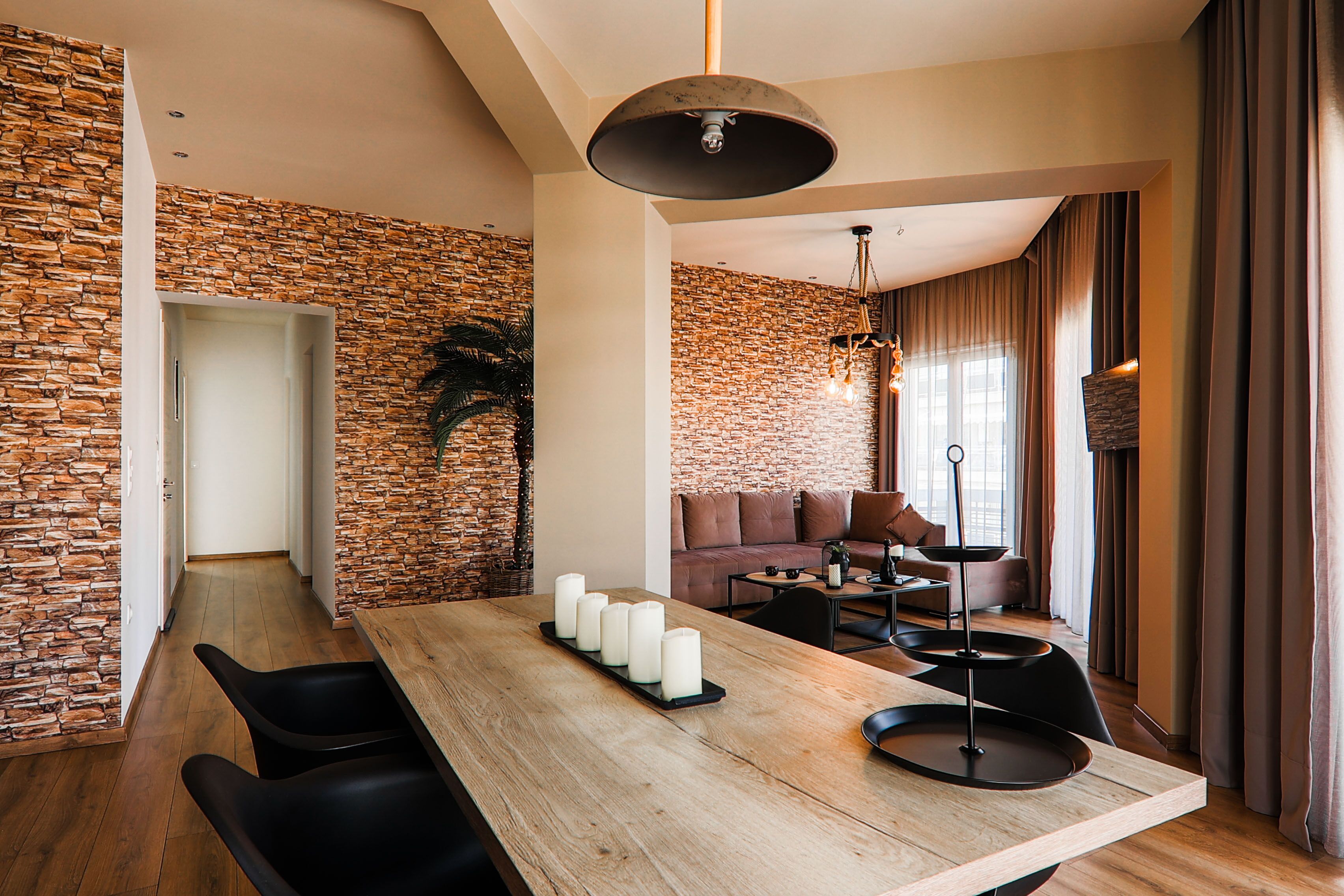 Ein modernes Wohnzimmer mit Steinwand, einem Holzesstisch mit Kerzen und einem schwarzen Sofa.