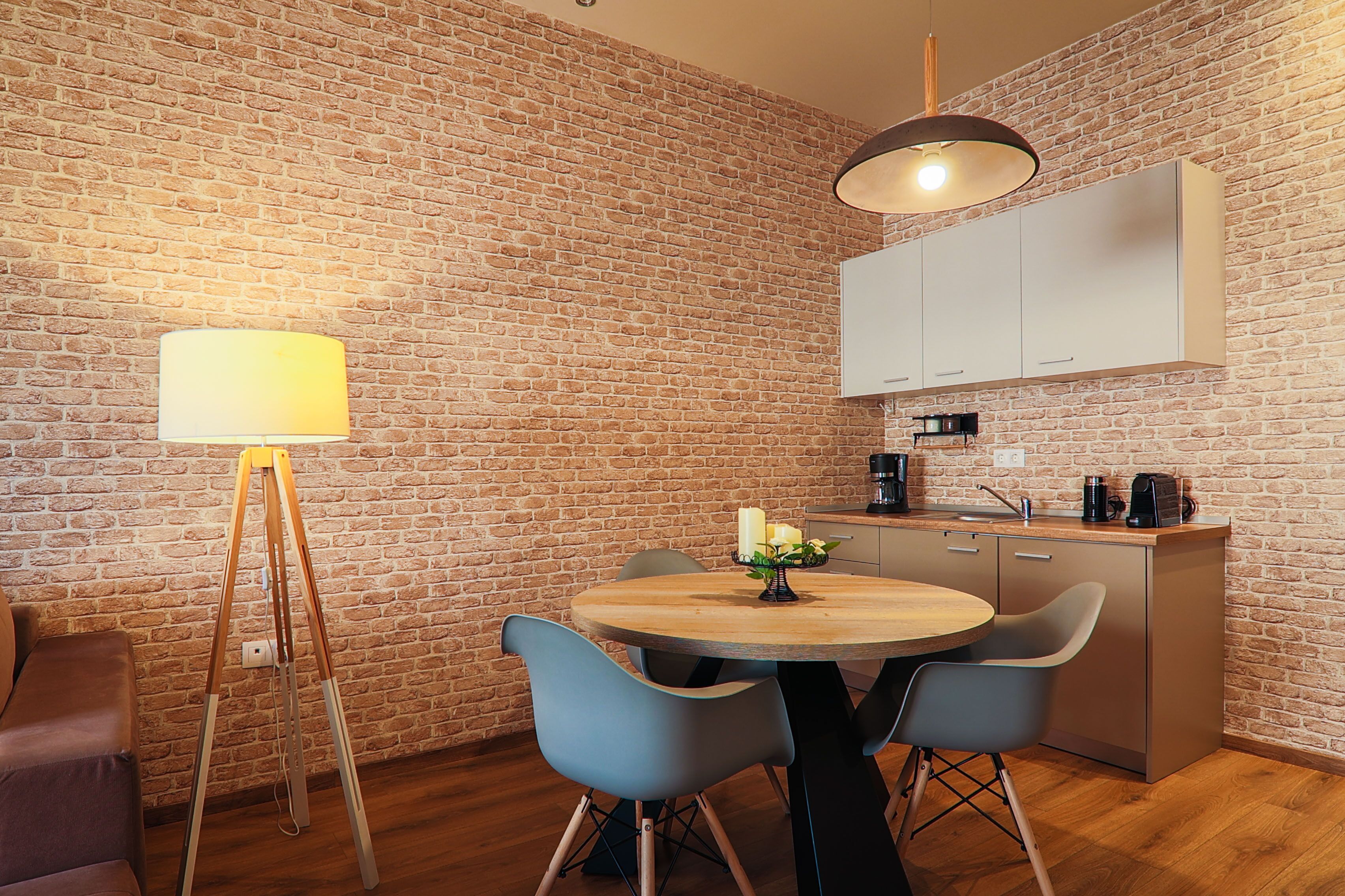 A modern kitchen with a brick wall, wooden cabinets, a round wooden table, and two chairs.