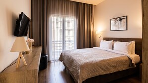 A hotel room with a bed, a TV, a lamp, and a window with curtains.
