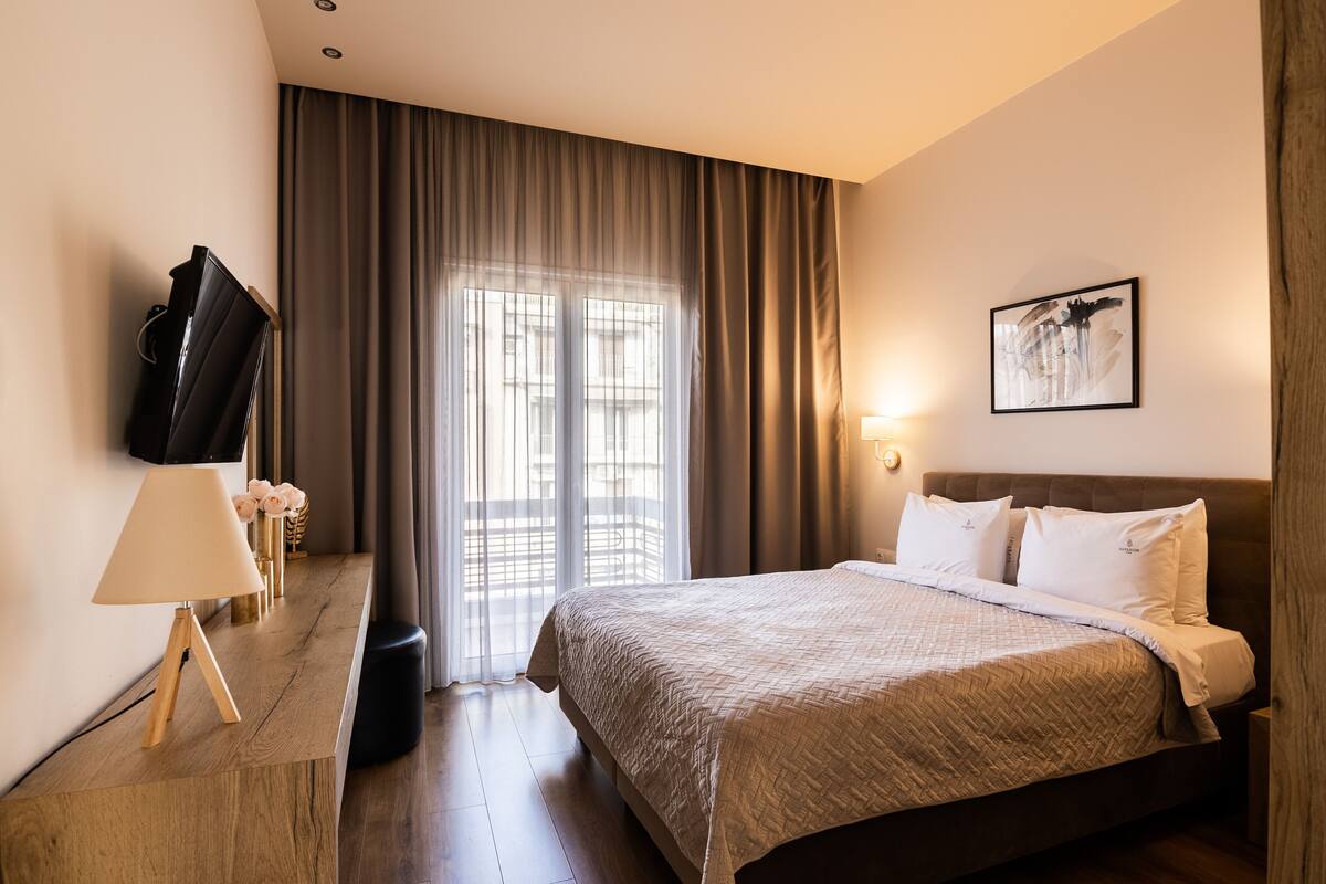 A hotel room with a bed, a TV, a lamp, and a window with curtains.