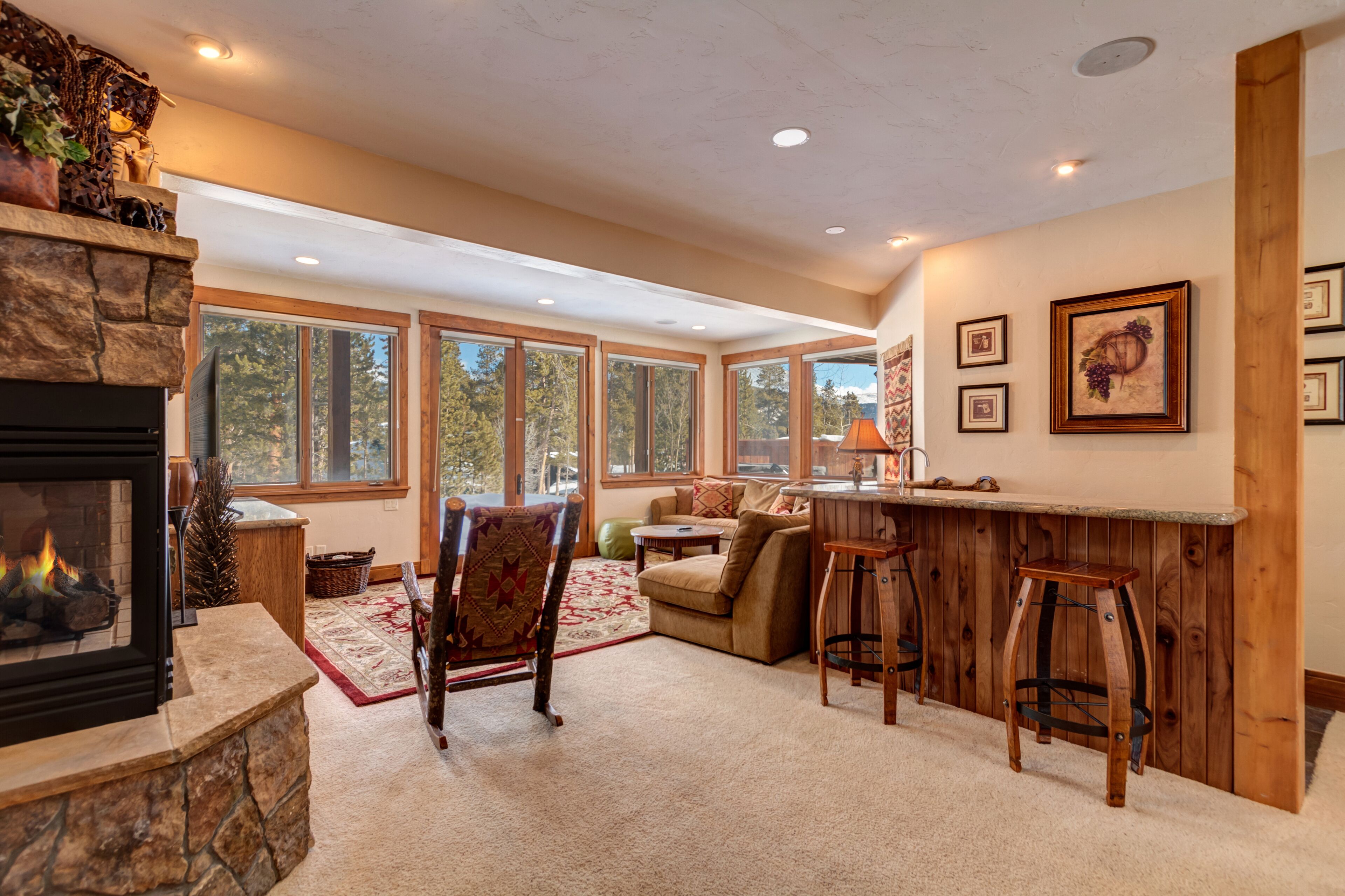 A spacious living area with a stone fireplace, large windows, a cozy seating area, and a wooden bar.