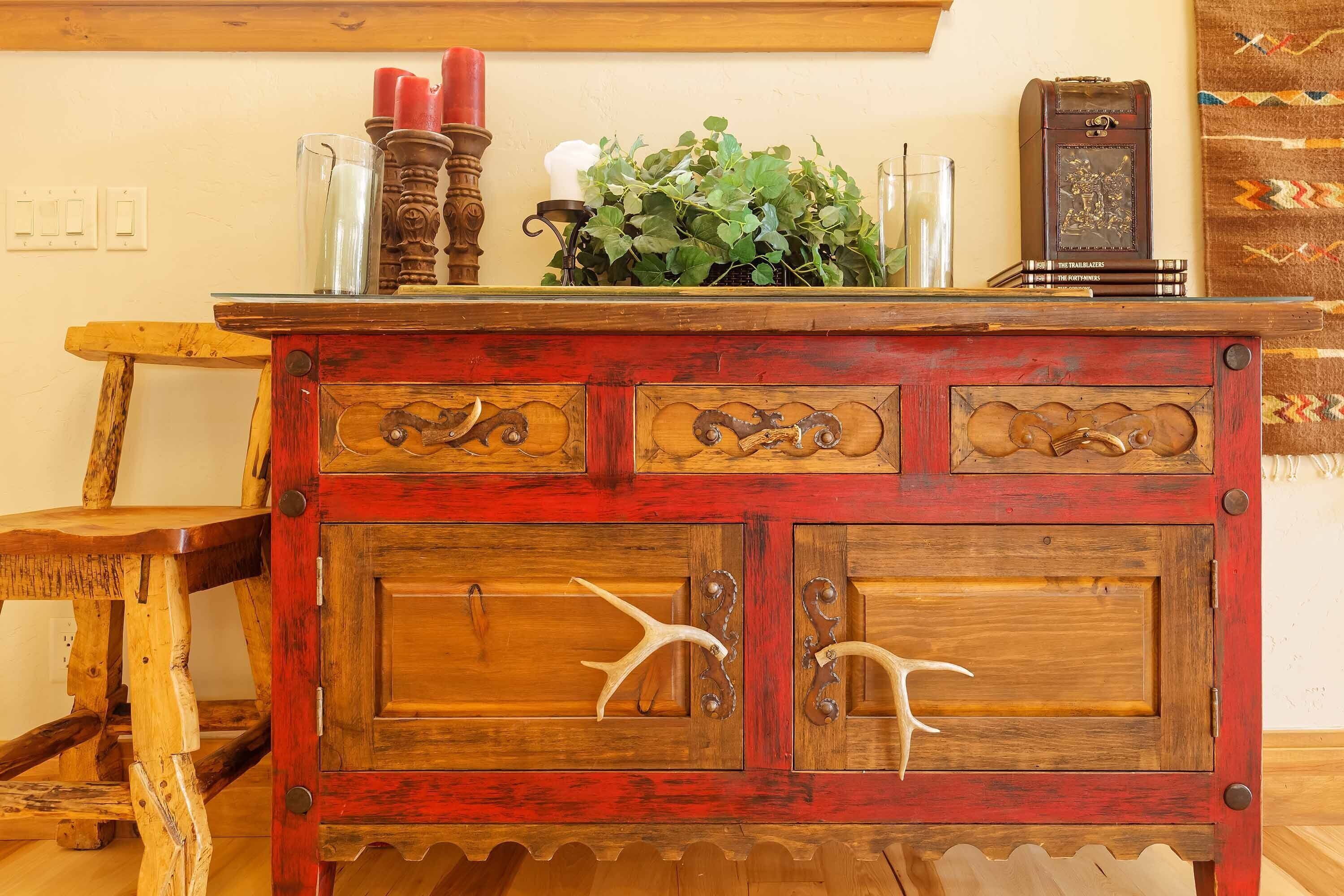 A rustic wooden cabinet with carved handles, a candle holder, and a plant on top.