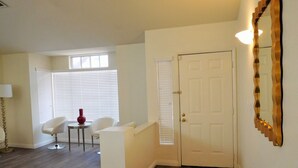 A hallway with a white door, a small table with a red vase, and a white chair. - Spacious New Remodel  Vacation Home (Las Vegas)