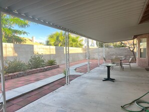 Un patio couvert avec un sol en béton, un chemin en briques et une table entourée de chaises.
