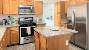 A kitchen with wooden cabinets, a stainless steel refrigerator, a microwave, a stove, and granite countertops. - Spacious New Remodel  Vacation Home (Las Vegas)