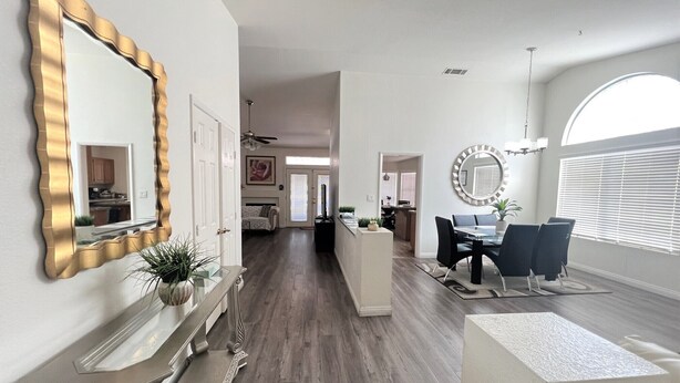 A modern living room with a dining area, a large mirror, and a view of the kitchen. - Spacious New Remodel  Vacation Home (Las Vegas)