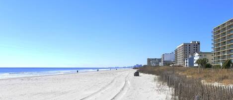 A beach with a sandy path leading to a building with multiple floors.